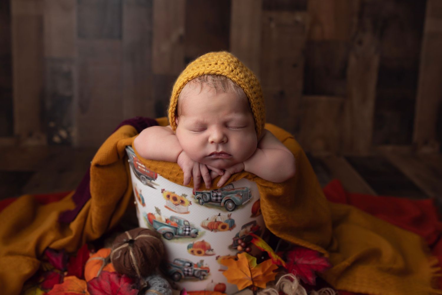 Sleeping baby in yellow hat and patterned outfit on orange blanket.