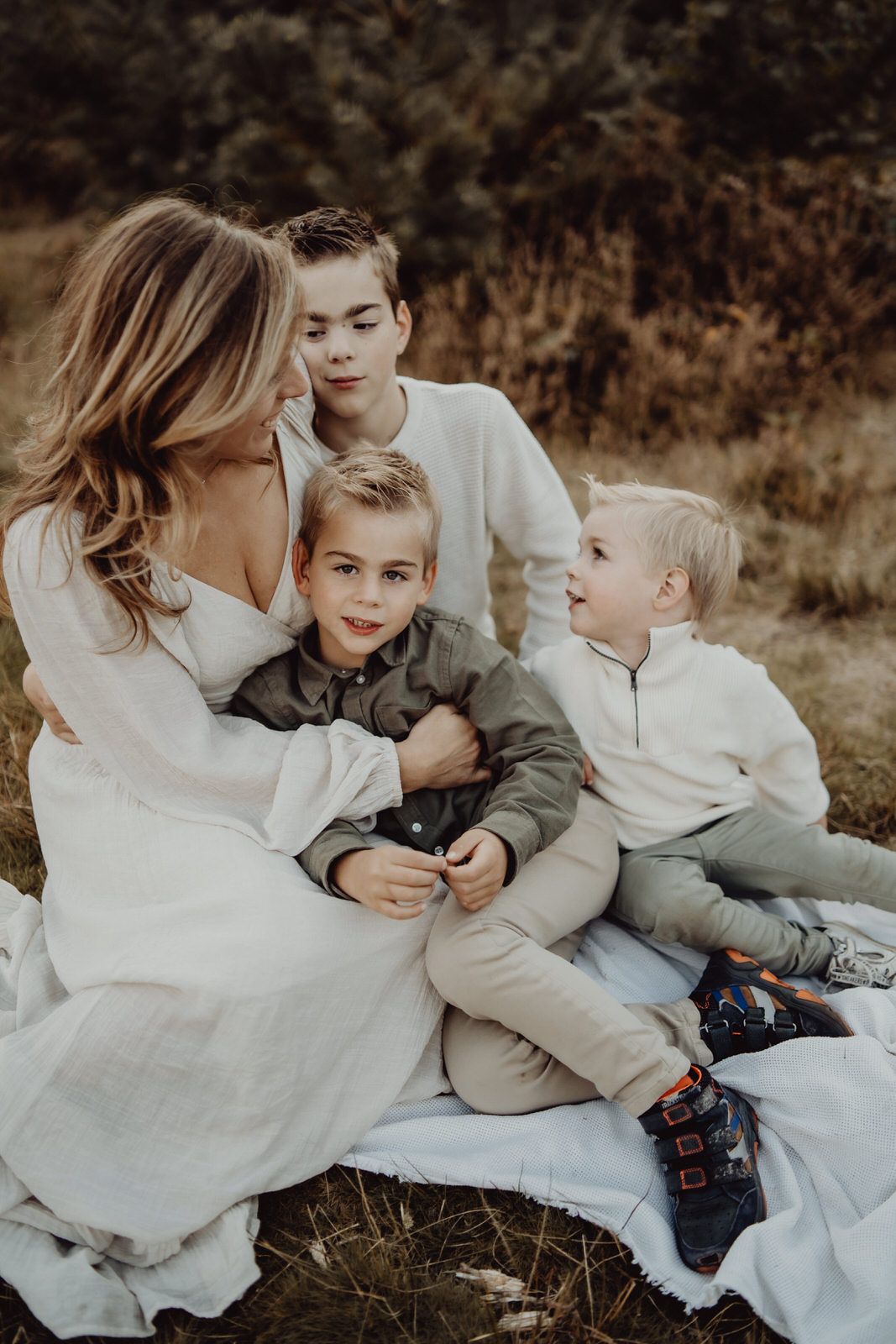 A family wearing coordinated white and neutral outfits sits together on a blanket outdoors.