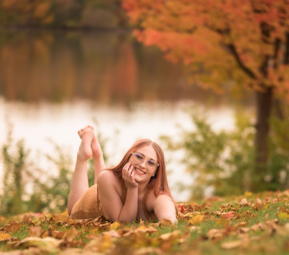 Autumn portrait session by lake with fall foliage reflecting in water.