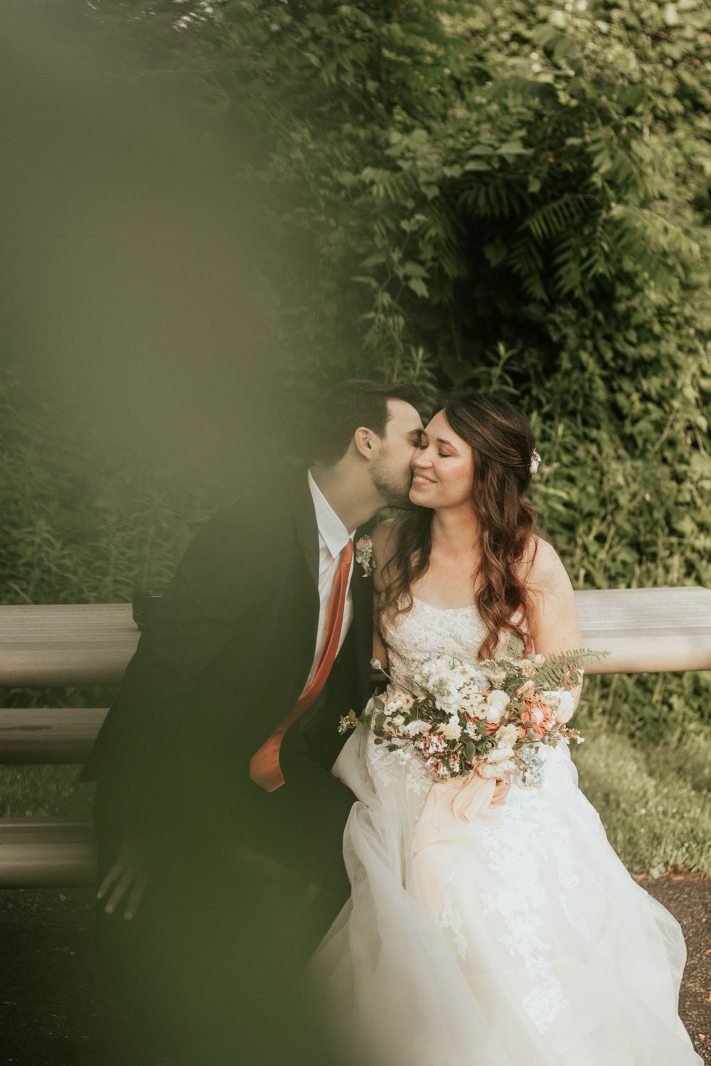 Romantic wedding portrait of a couple embracing outdoors with greenery in background.
