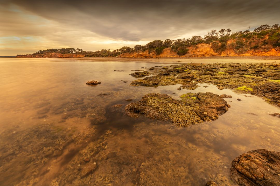 Rocky coastal landscape with orange cliffs and tidal pools during golden hour.