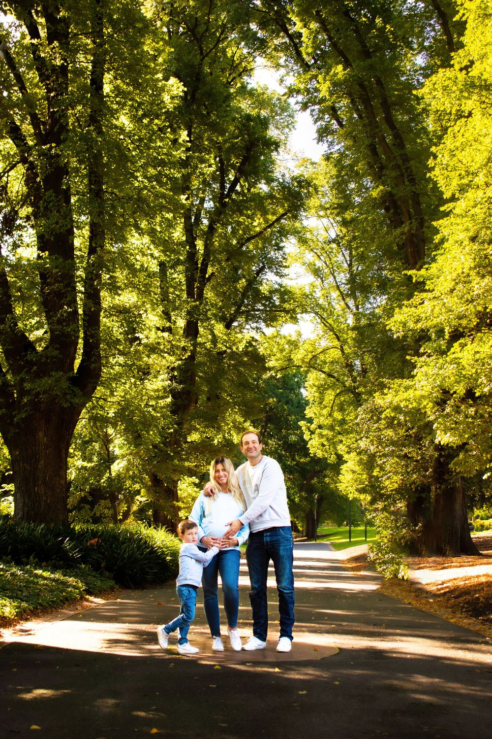 A family walking together on a tree-lined path during a sunny autumn day.