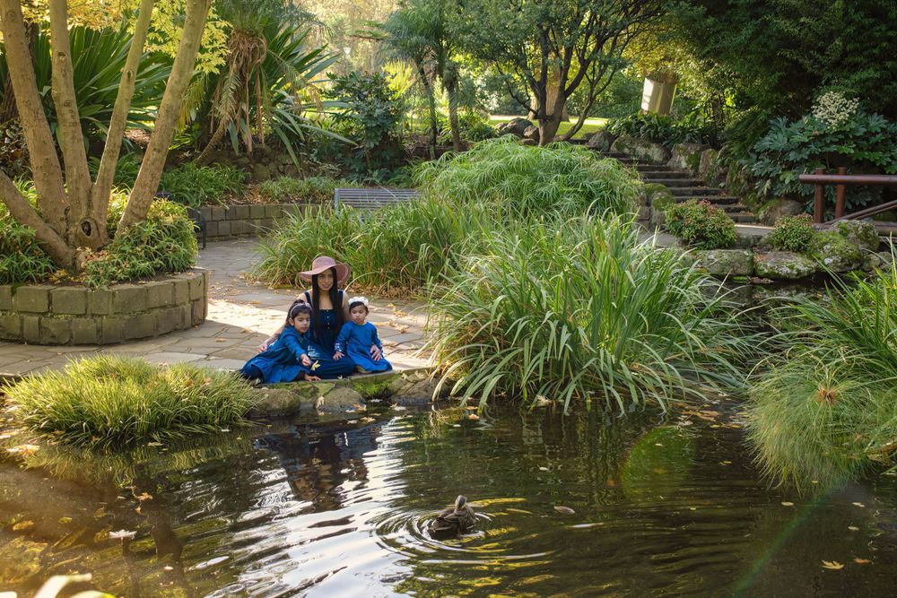 A scenic garden path with a wooden bridge over a tranquil pond surrounded by greenery.