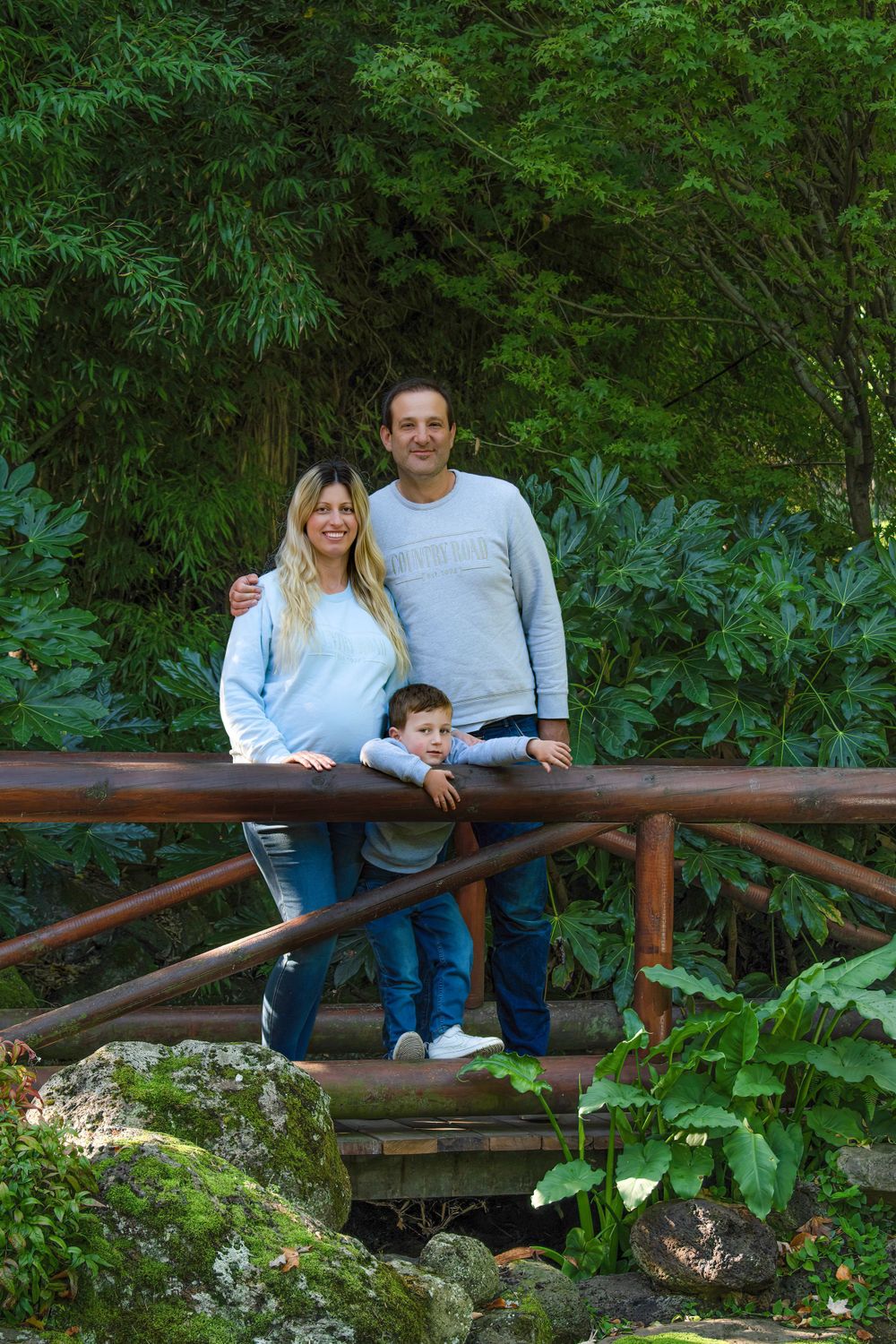 Family sitting together on a rustic wooden bridge surrounded by lush garden foliage.