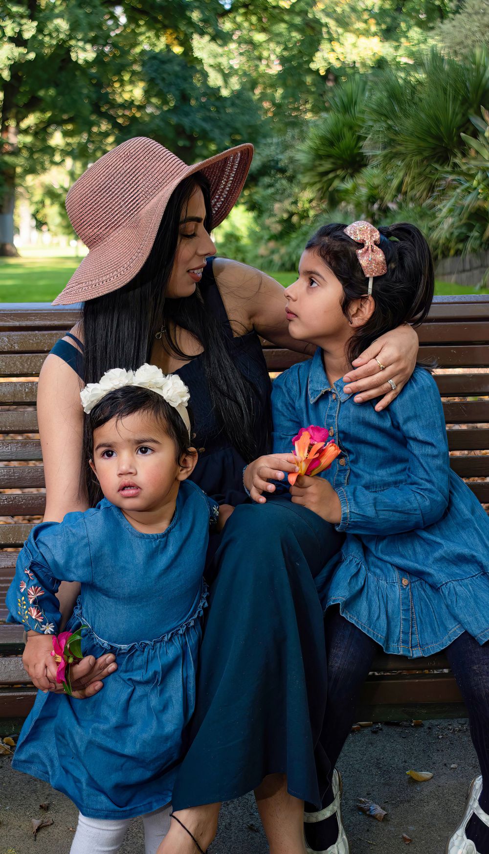 A mother and child share intimate moments sitting on a park bench in matching blue outfits.