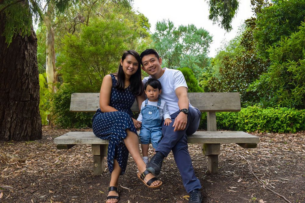 Family sitting together on wooden bench in lush green park setting.