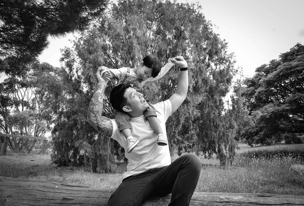 Black and white image of parent joyfully lifting child in outdoor park setting.