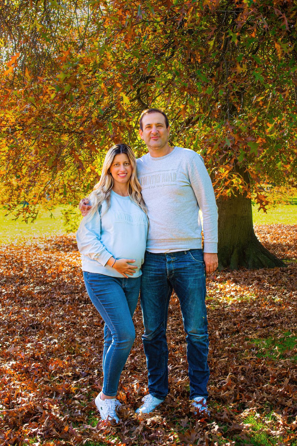 A couple posing for photos among fall leaves wearing coordinated casual outfits.