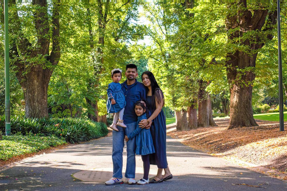 Family walking together on a tree-lined path in coordinated blue outfits on a sunny day.