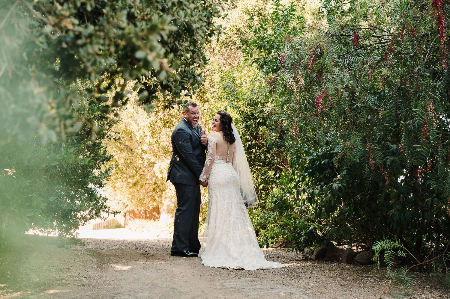 A wedding couple stands surrounded by lush greenery in a garden setting during golden hour.