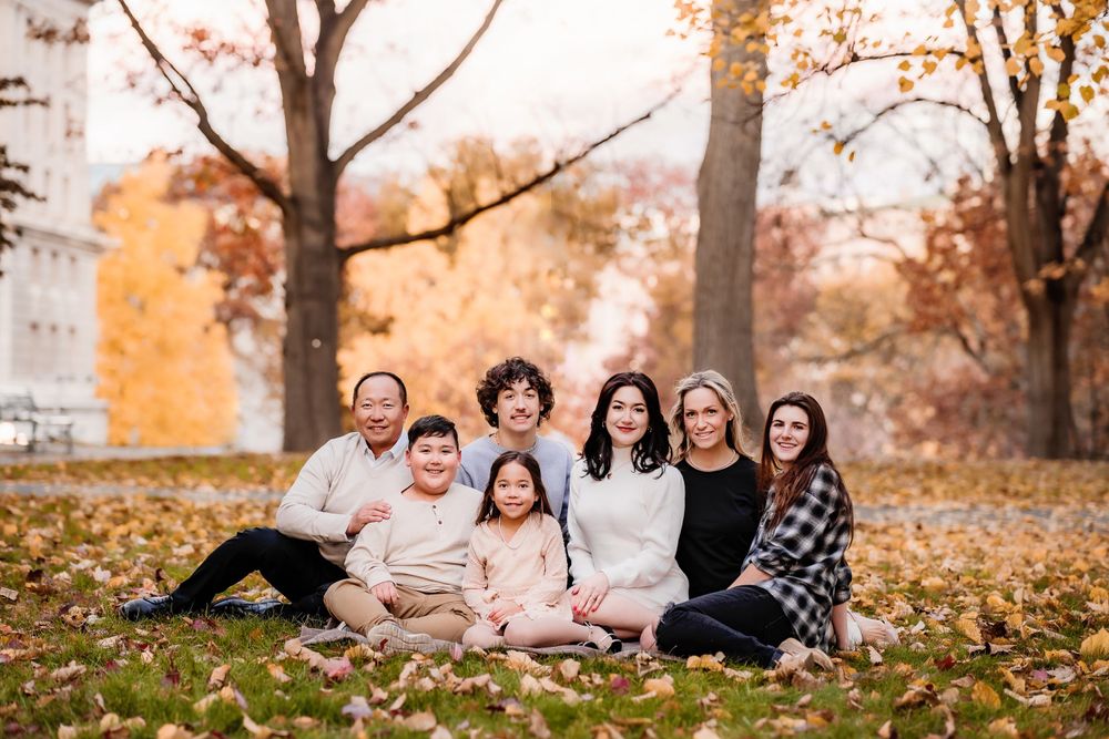 Family group portrait sitting together on fallen autumn leaves in park setting.