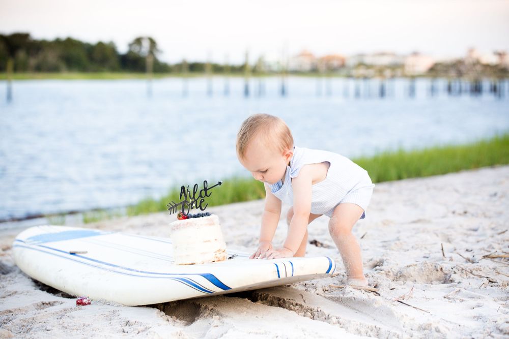 Small baby exploring paddleboard on sandy beach near waterfront.