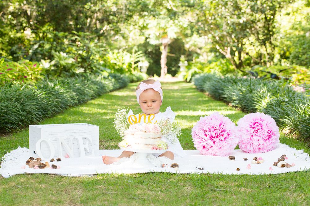 Garden party setup with white blanket, pink flowers and birthday cake on sunny day.