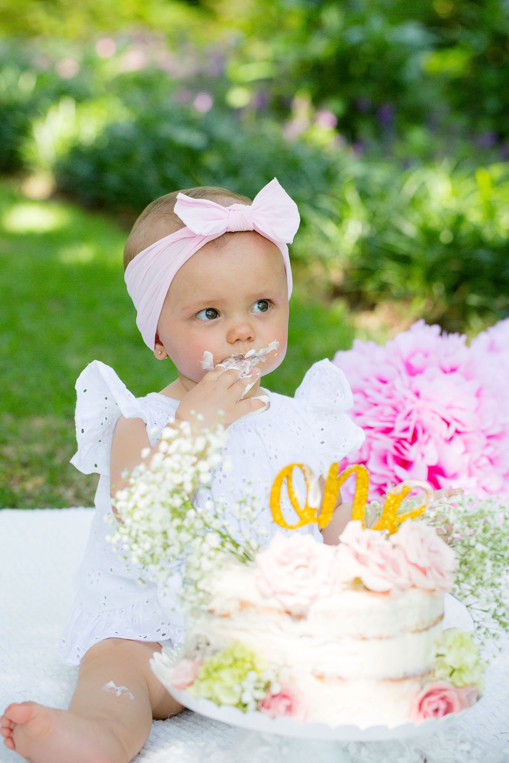 First birthday cake smash setup in garden with white and pink decor.