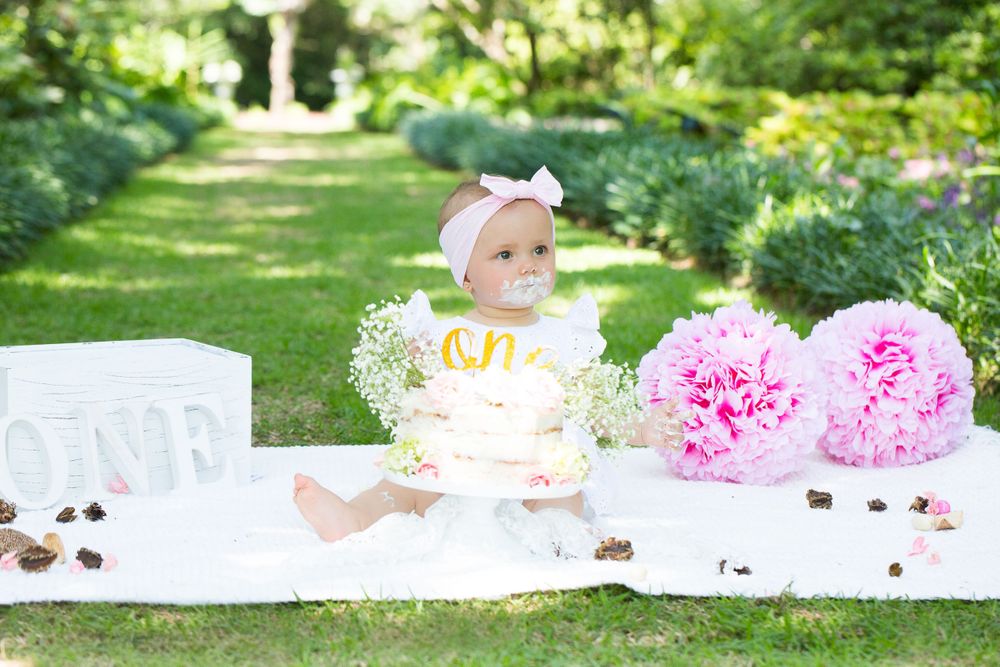 Outdoor cake smash setup with pink peonies and white blanket on grass.