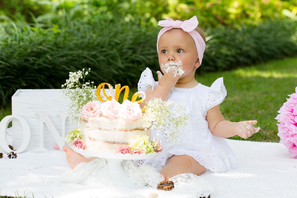First birthday celebration with decorated cake and pink peonies in garden setting.