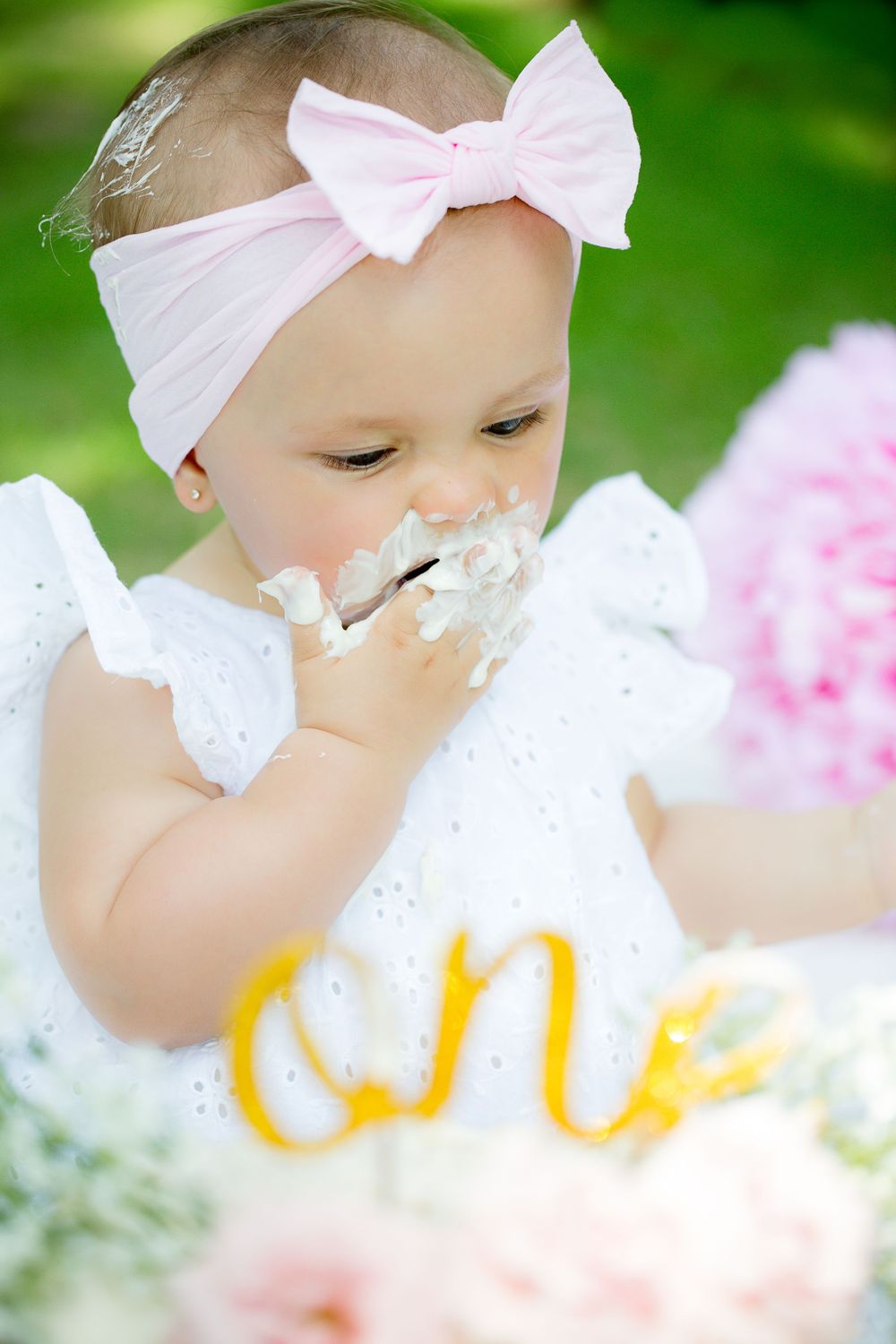 Close-up of cake smash moment with white dress and pink bow.