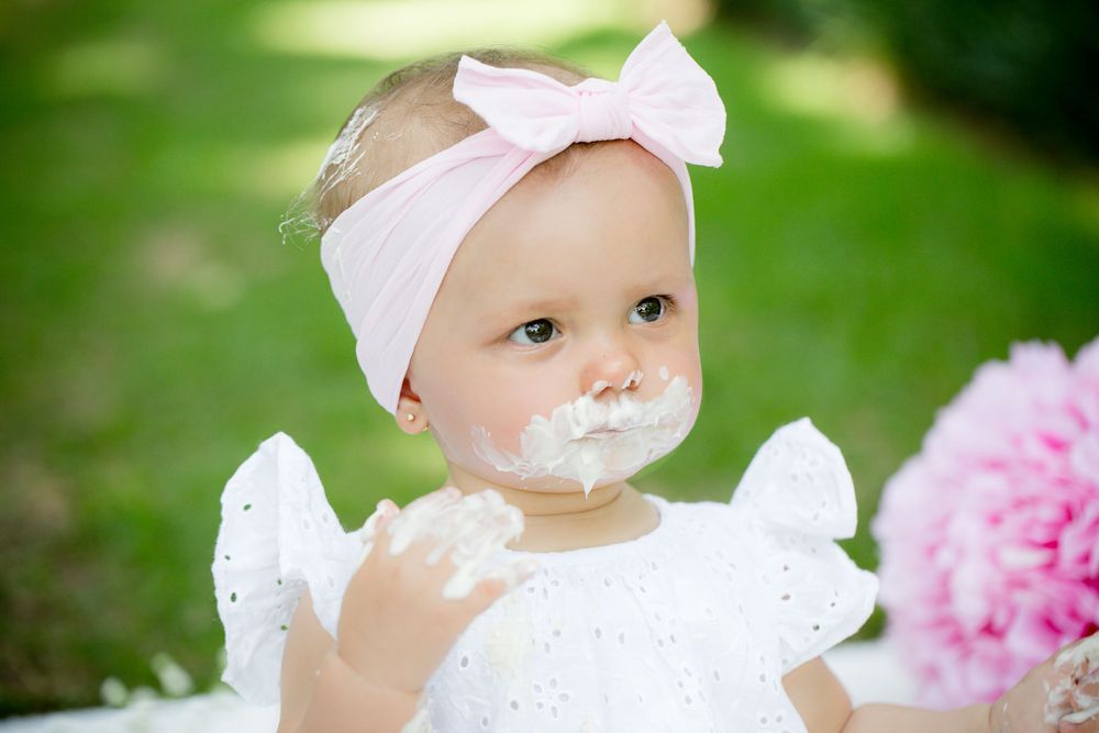 Sweet cake smash portrait with pink bow and white dress.