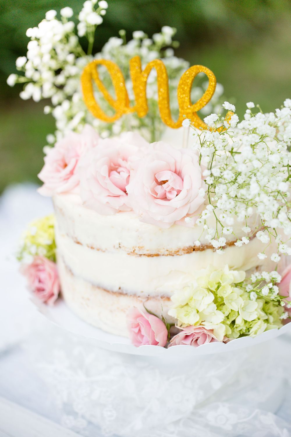 Naked cake decorated with pink roses, baby's breath and gold 'ONE' topper.
