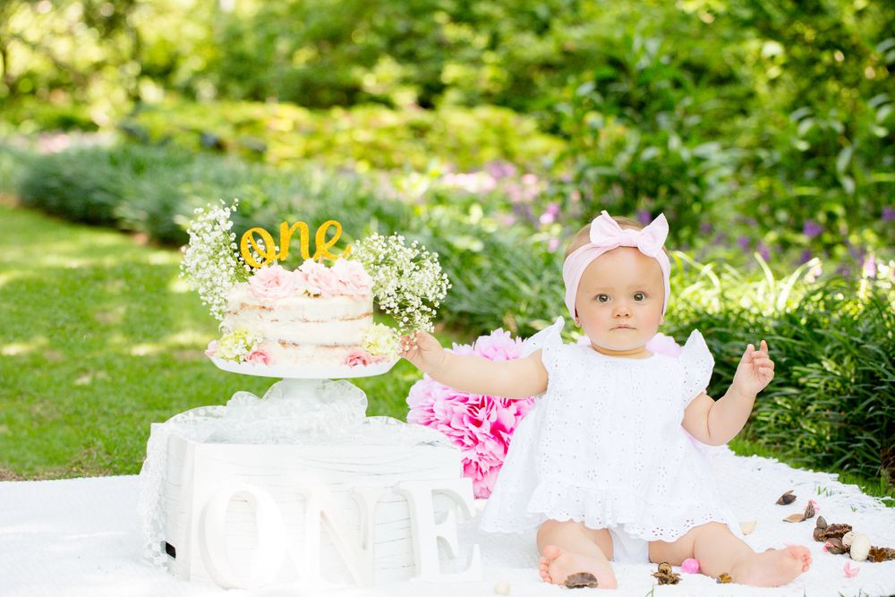 Garden birthday setup with naked cake, pink flowers and white decor.