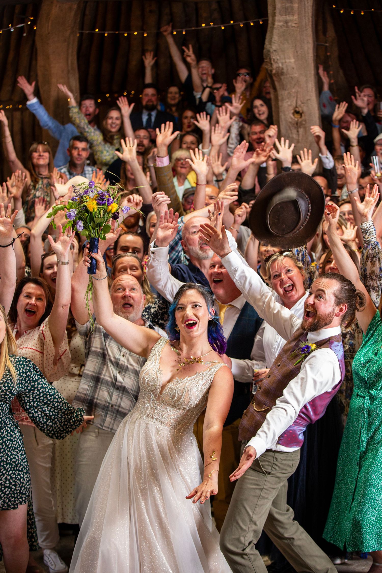 Wedding guests raise their hands in celebration inside a rustic wooden barn venue.