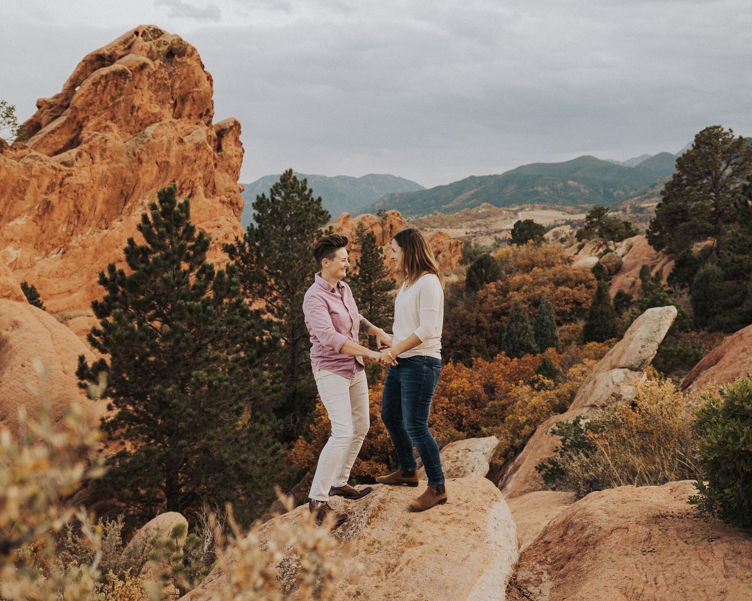 two women smiling at each other while holding hands surrounded by nature and mountains in the background