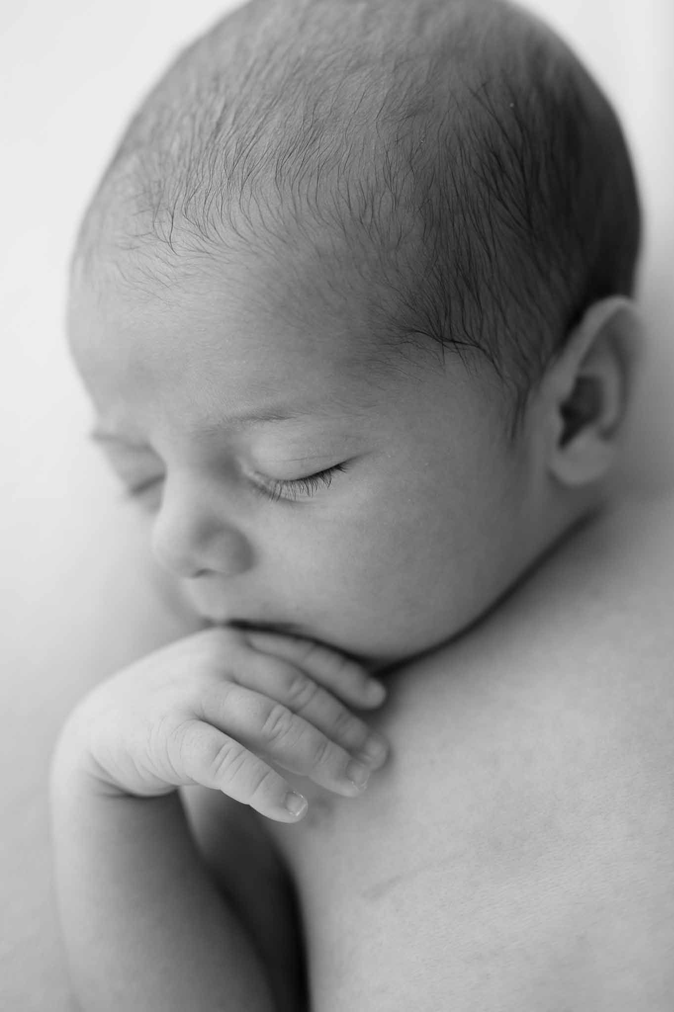 Close-up black and white portrait of sleeping newborn with hand near face.