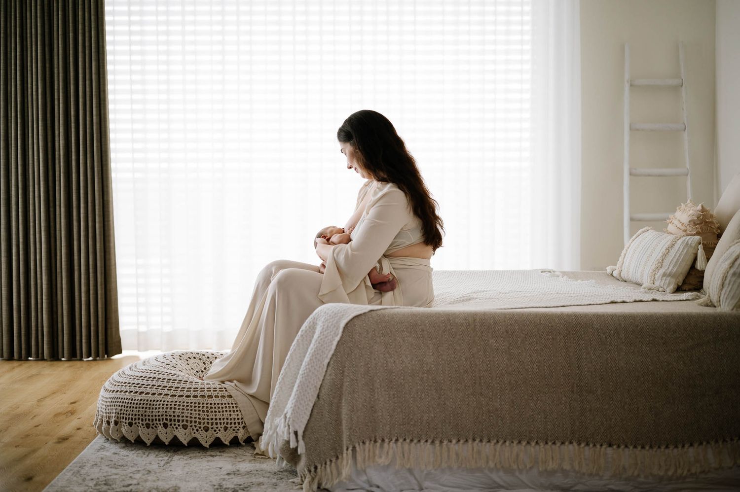 Serene portrait of expectant mother sitting on bed in sunlit room with modern decor.