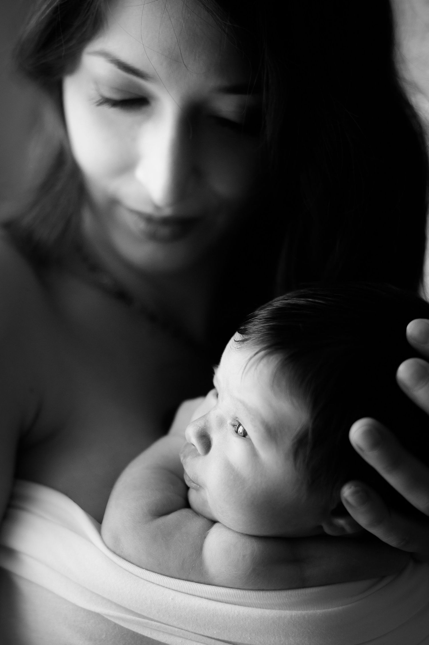 A tender black and white portrait of a parent cradling a newborn baby in soft natural light.