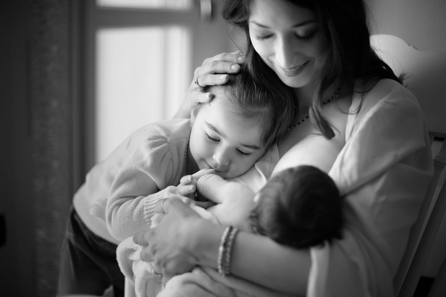 An intimate family moment showing a parent and child holding a newborn baby in black and white.