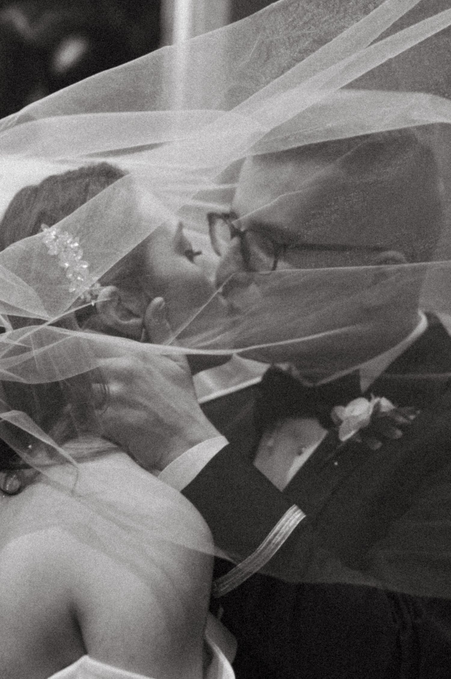 Romantic black and white wedding photo showing a tender kiss through delicate bridal veil.