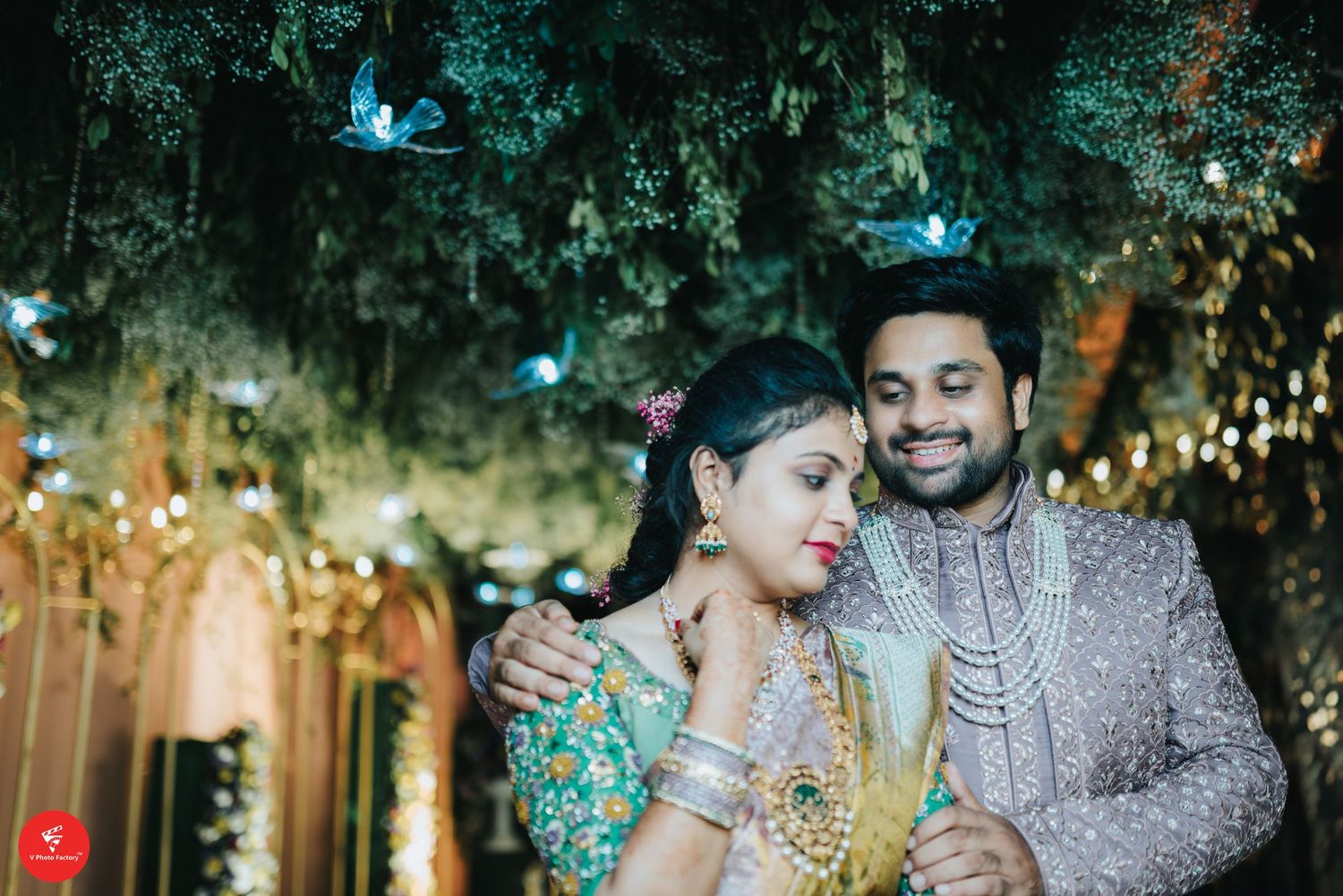 Romantic couple in traditional Indian attire share a tender moment under twinkling lights and blue butterflies at their reception.