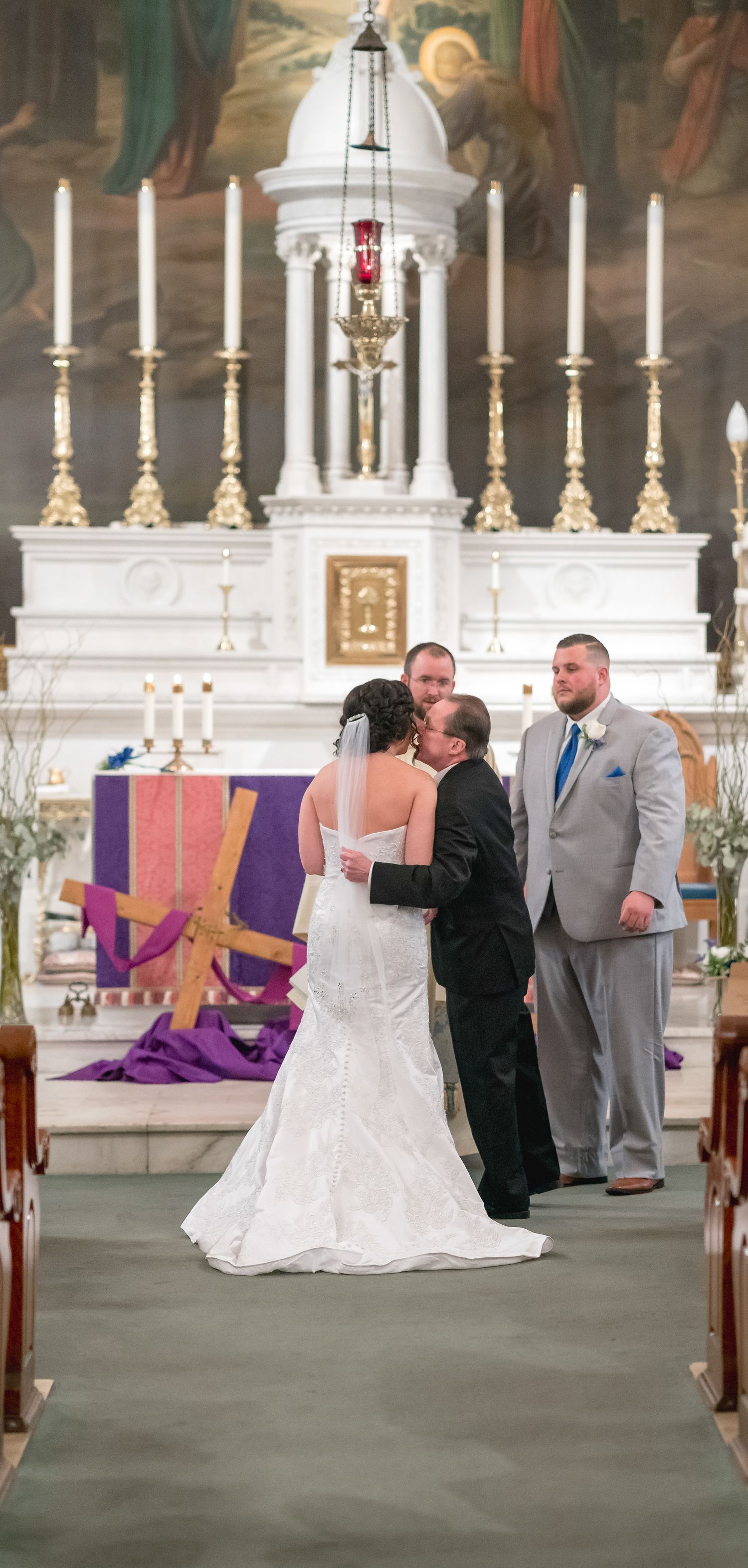 Wedding ceremony in a traditional church with ornate white altar and purple decorative elements.