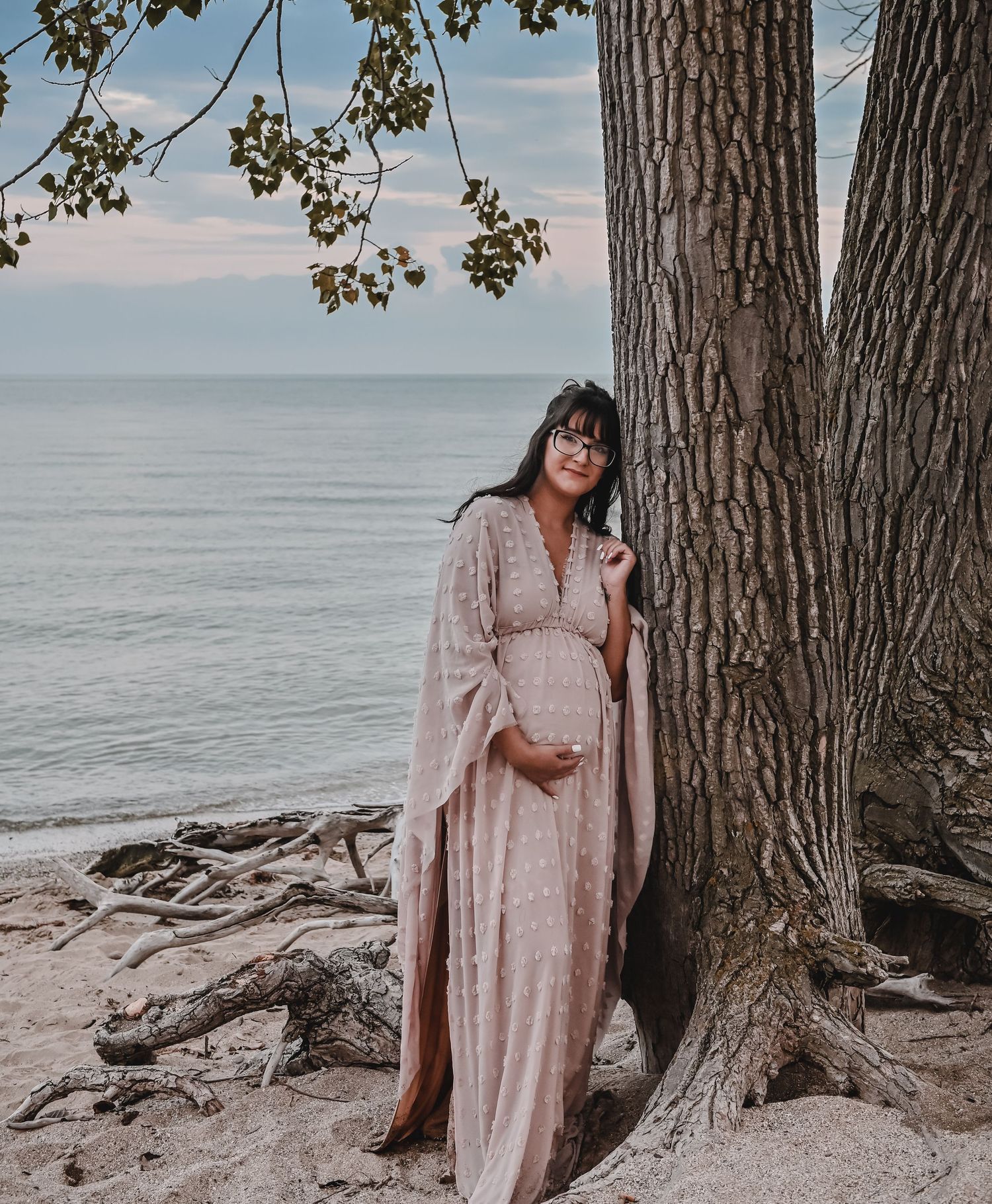 A maternity photo of a woman in a flowing pink dress by the ocean.