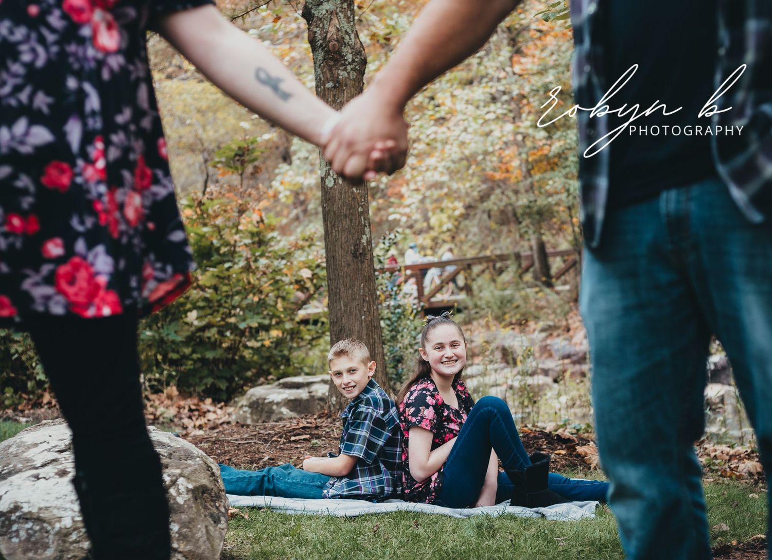 A couple sitting on a blanket in autumn woods while holding hands in the foreground creates a romantic scene.