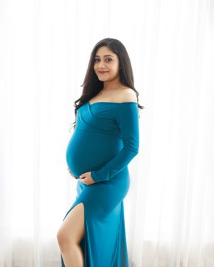 Bright maternity portrait in turquoise off-shoulder dress against white background.