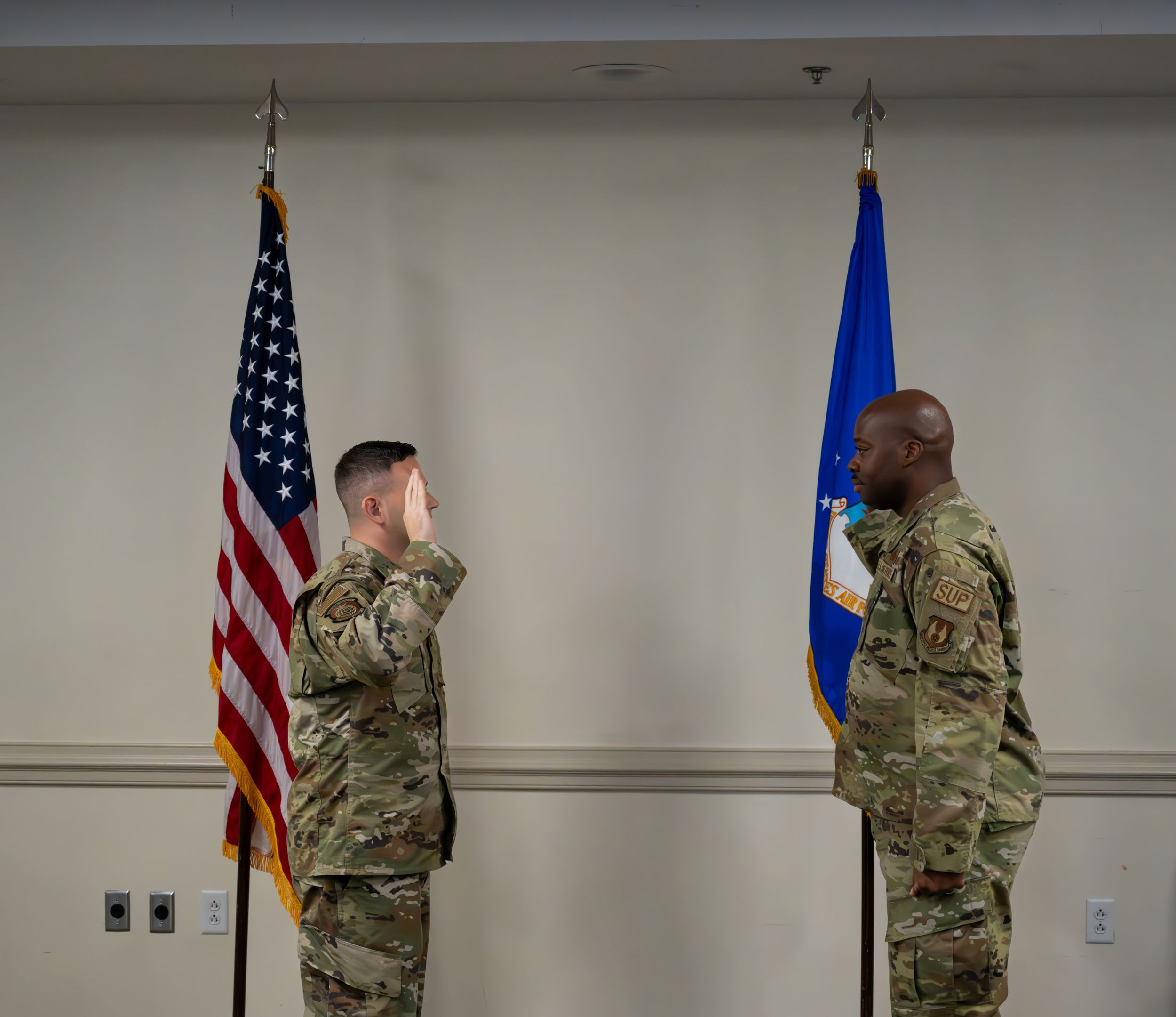 Two service members stand at attention by US and Air Force flags.