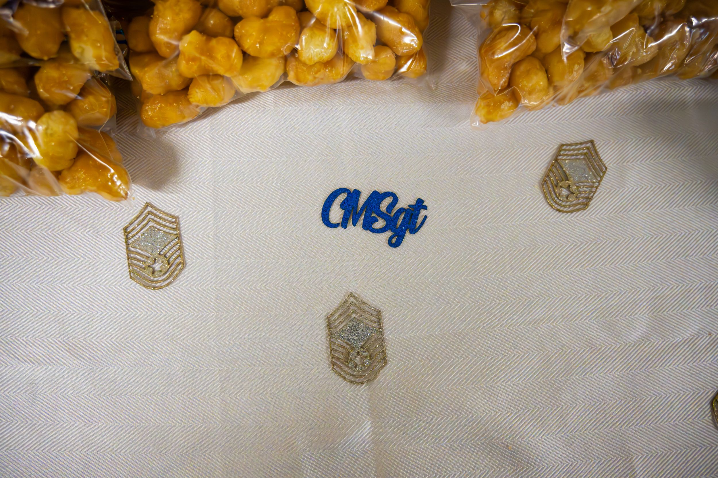 Yellow pastries are arranged in rows on a white tablecloth at a military gathering.