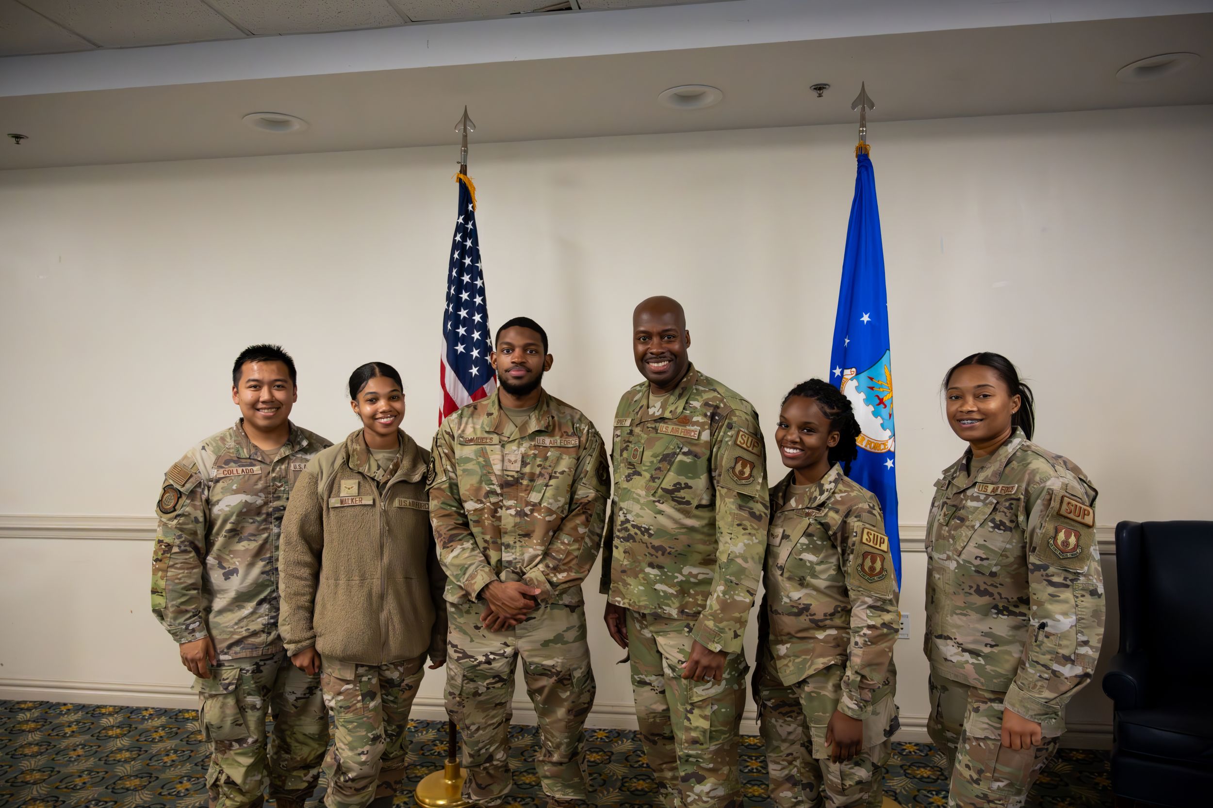 Group of military personnel pose together for formal photo with US and Air Force flags.