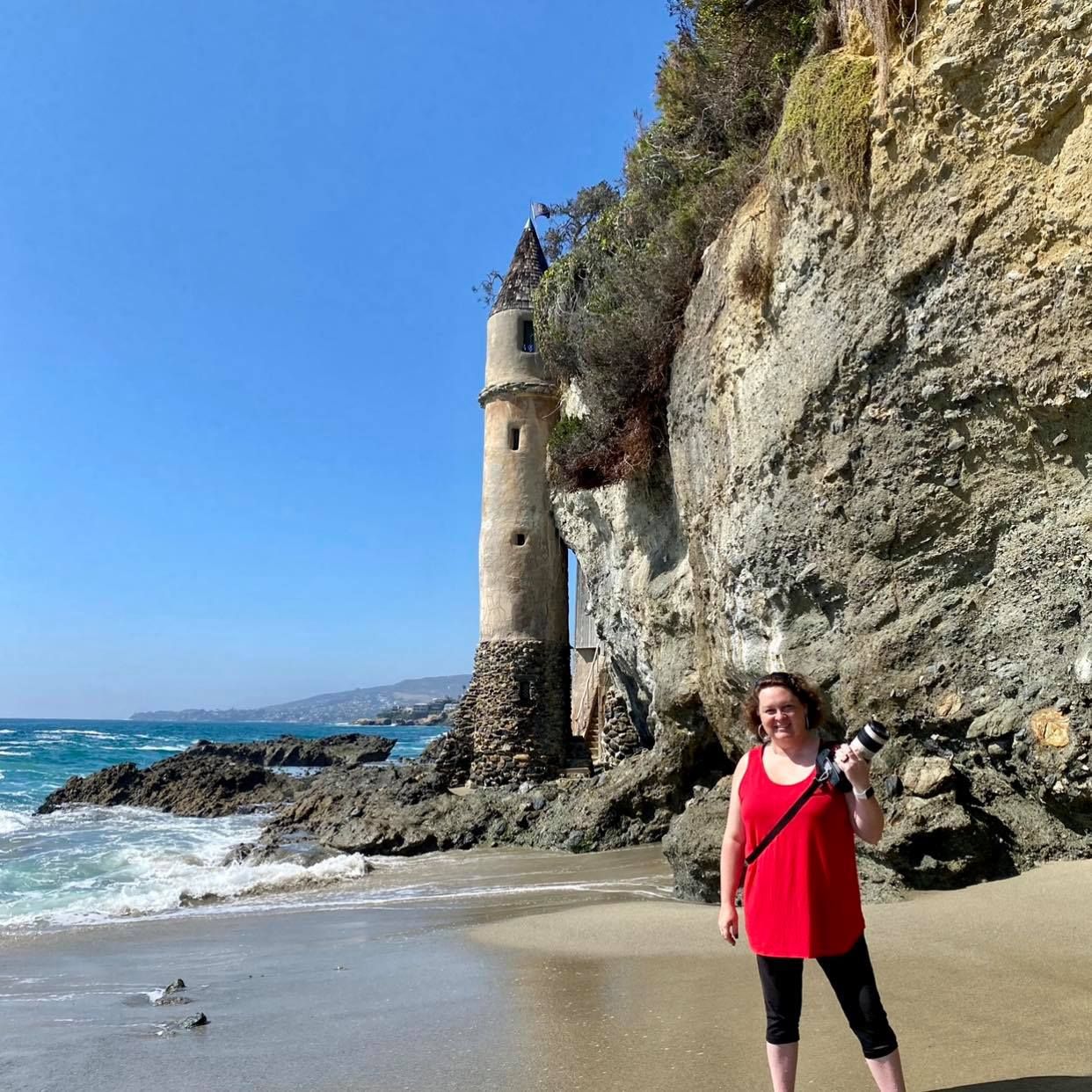 Leslie Sessums, photographer with camera in hand, in front of Victoria Beach Pirate Tower in Laguna Beach, California on a sunny day