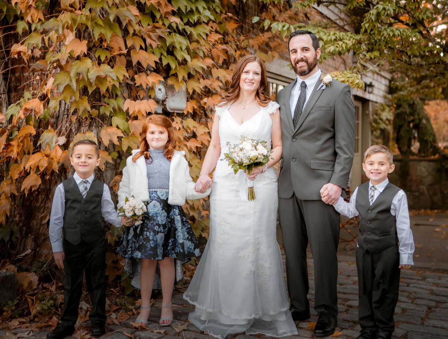 Wedding party portrait with fall foliage backdrop and children in formal attire.