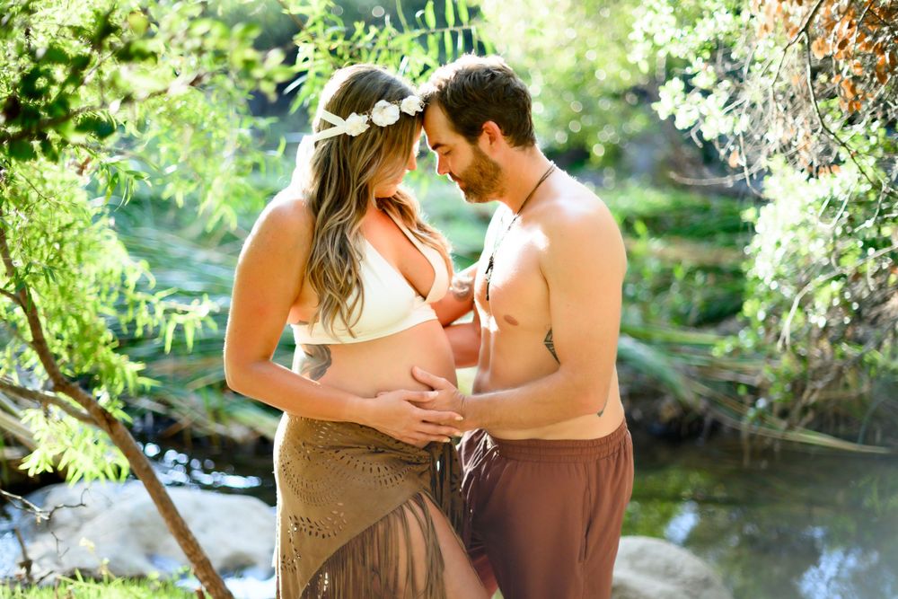 Couple embraces tenderly during maternity photoshoot in a lush forest setting. Maternity photo session in Las Vegas. Maternity photographer