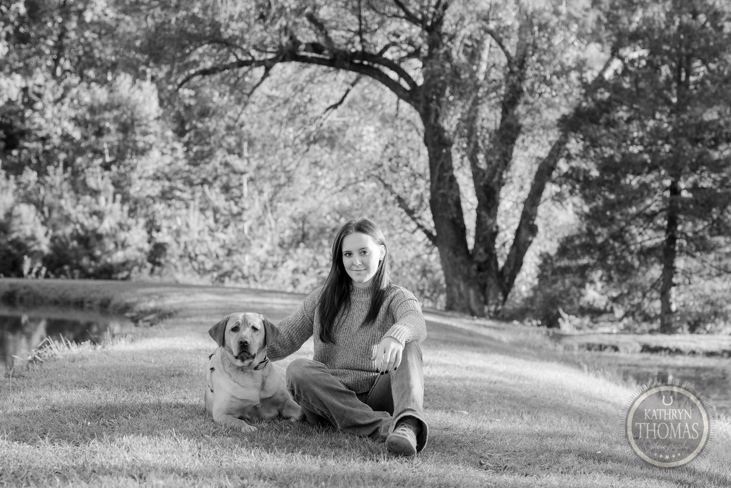 Black and white portrait featuring a golden retriever and their companion sitting in a park setting.