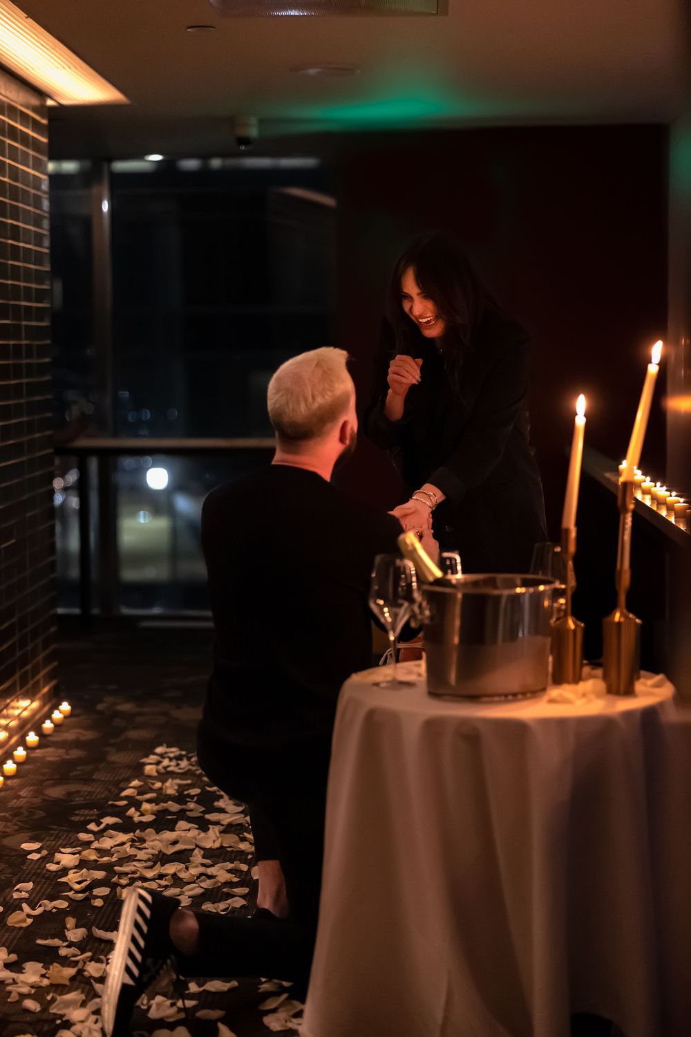 A candlelit proposal scene with rose petals scattered around a decorated table.