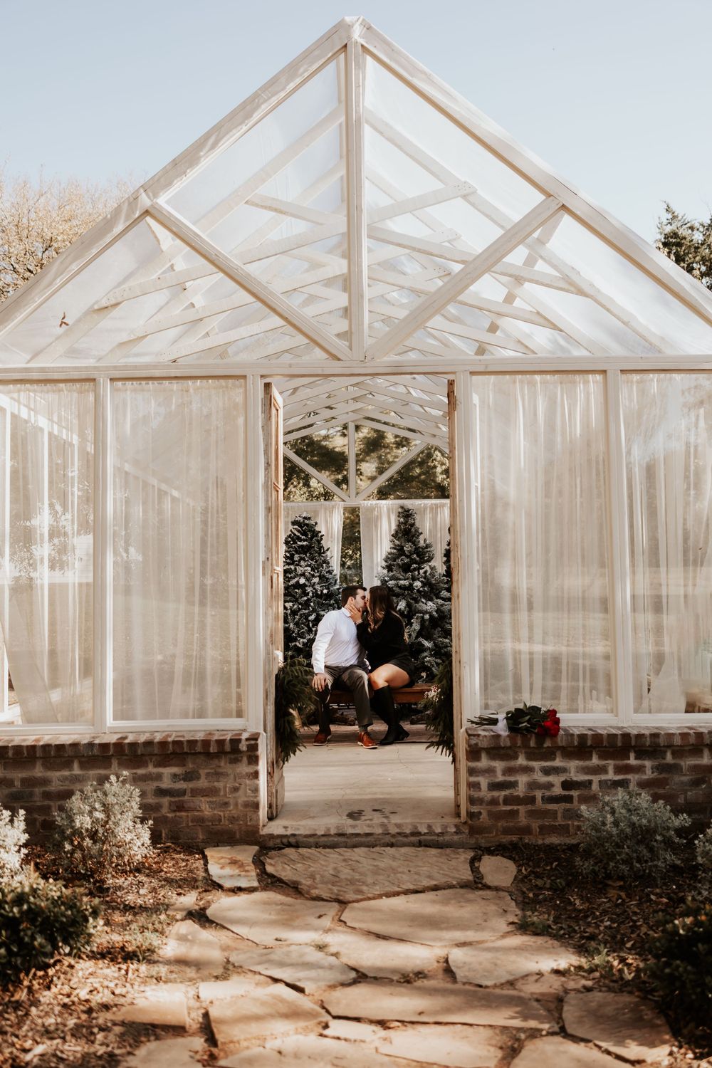 A white greenhouse with glass panels and brick foundation captured during golden hour.