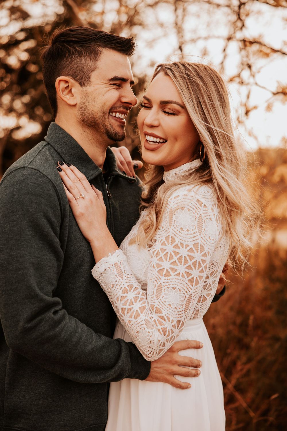 A joyful engagement photo showing a couple laughing together in warm autumn sunlight.