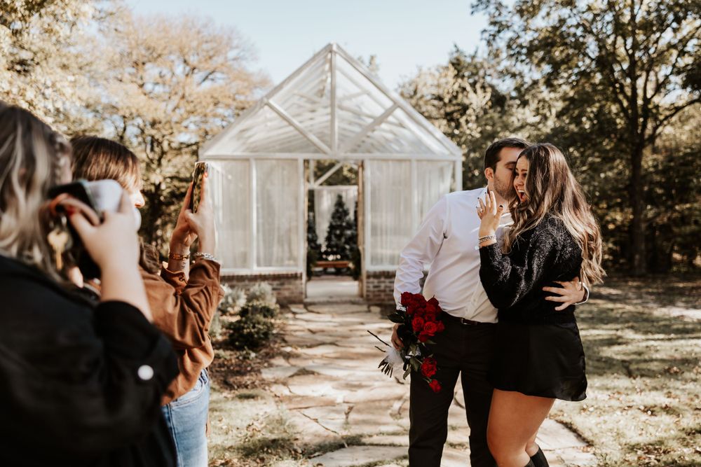 A photographer captures a couple's moment outside a white greenhouse structure.