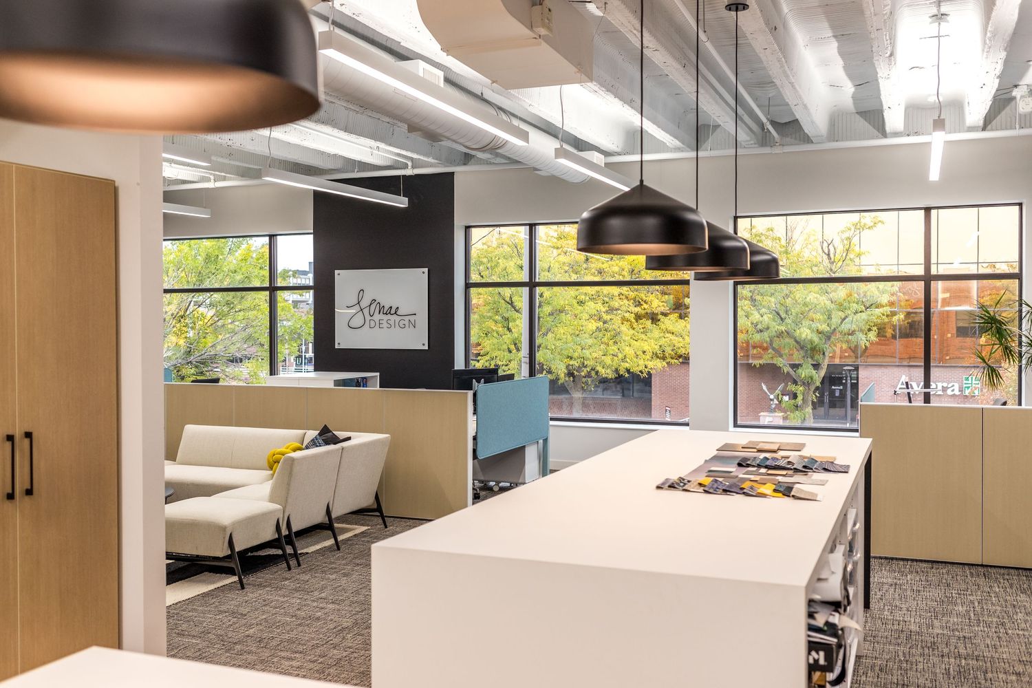 Modern office breakroom with white counters, pendant lights, and comfortable seating area near windows.