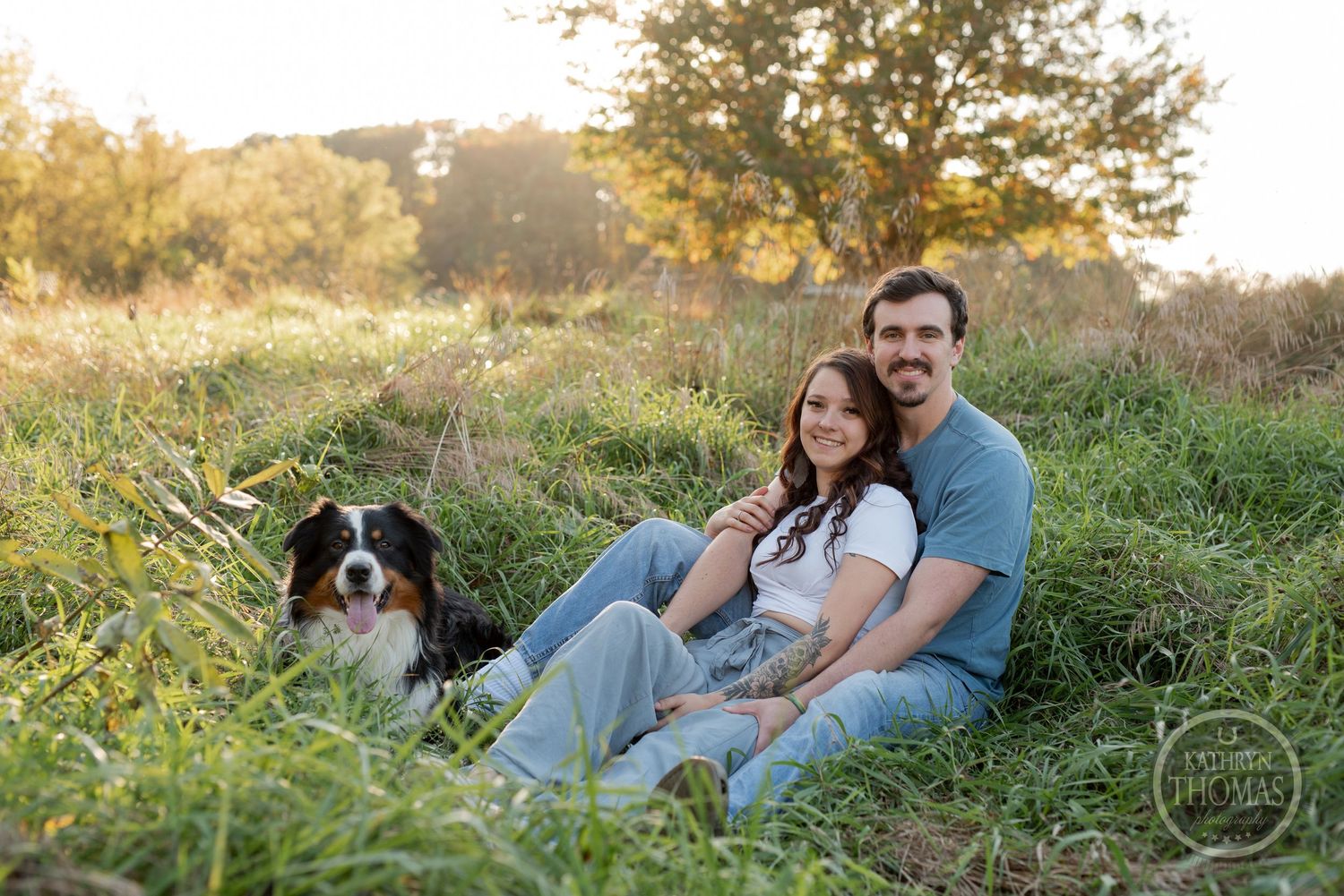 A couple relaxes in a grassy field with their Border Collie during golden hour.