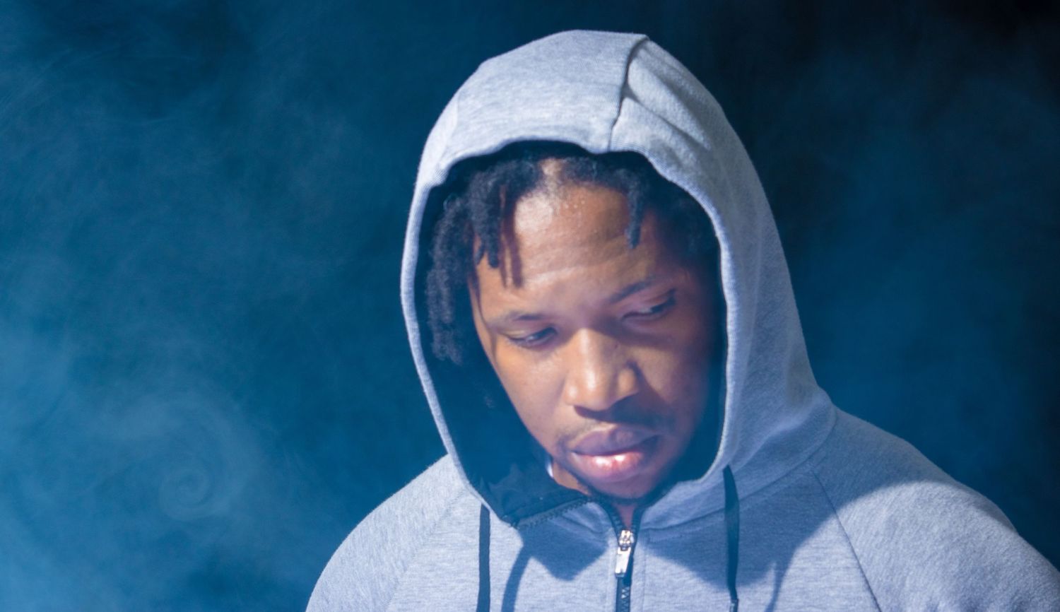 Person wearing a gray hoodie looking downward against a smoky dark blue background.